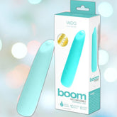 Displayed in its "VeDO Boom" packaging, the Turquoise VeDO Boom Rechargeable Warming Bullet Vibrator features multiple modes and is designed for versatility with submersible capabilities. The blurred, multicolored lights in the background highlight its alluring appeal.